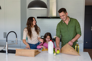 Happy caucasian parents and daughter unpacking groceries in kitchen - obrazy, fototapety, plakaty