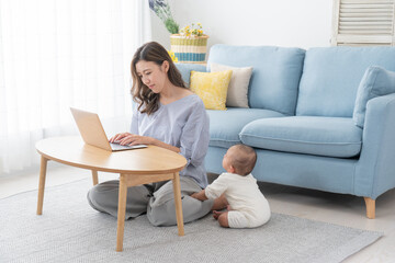パソコンで仕事しながら赤ちゃんの面倒を見る女性（育児・子育て・家族・ファミリー）