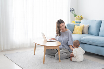 パソコンで仕事しながら赤ちゃんの面倒を見る女性（育児・子育て・家族・ファミリー）