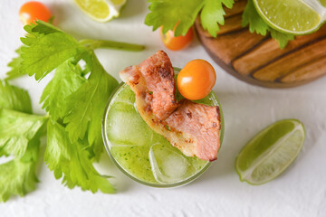 Glass of bloody Mary cocktail garnished with bacon on light background