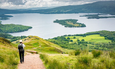 a view of Loch Lomond from the West highland Way in Scotland. A hiker walking on the path down to the lake. - 458630124