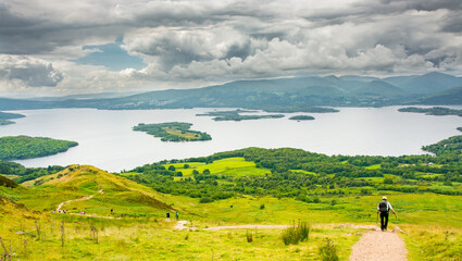 a view of Loch Lomond from the West highland Way in Scotland. A hiker walking on the path down to the lake. - 458630126