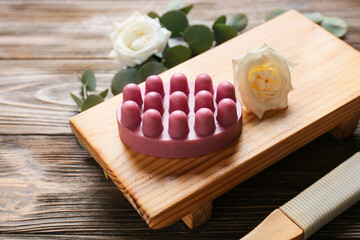 Board with massage soap bar and flower on wooden background, closeup