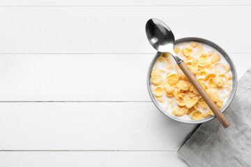 Bowl of tasty cornflakes with milk and spoon on light wooden background