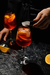 Female bartender preparing tasty aperol spritz cocktail on dark background, closeup