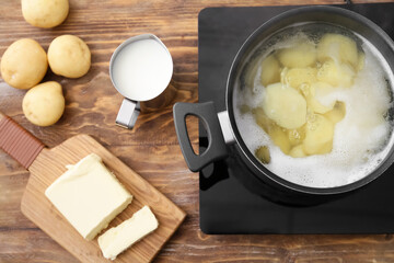 Fresh products and pot with boiling potatoes on electric stove at kitchen