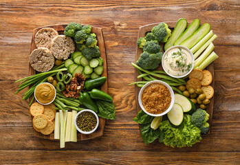 Boards with different green vegetables, rice crackers and bowls with sauce on wooden background