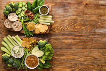 Fototapeta na wymiar Boards with different green vegetables, rice crackers and bowls with sauce on wooden background