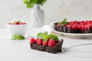 Spatula with piece of tasty raspberry pie and mint on light wooden table, closeup