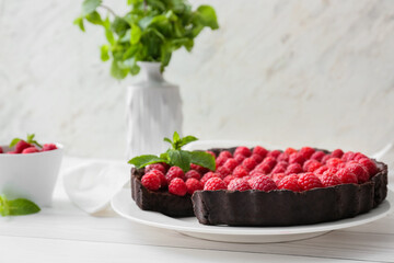 Plate with tasty raspberry pie and mint on light wooden table, closeup