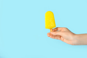 Female hand with tasty pineapple popsicle on color background