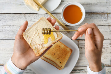 Woman preparing tasty toasted bread with honey on white wooden background