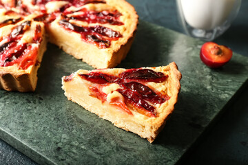Board with piece of tasty plum pie on dark background, closeup