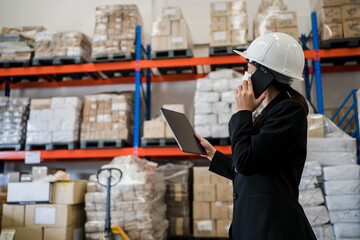 Manager wearing a protective face mask in black suit look confident using smartphone and digital tablet management goods in an interior factory warehouse, smart logistic industry concept..