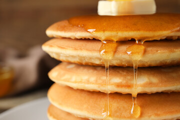 Tasty pancakes with honey and butter on table, closeup