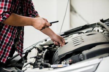 Close up of automotive mechanics using smartphone while checking engine room in the garage, auto...