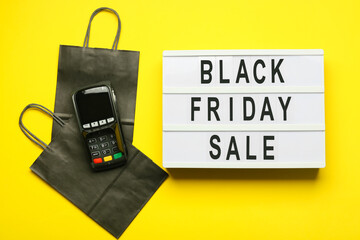 Shopping bags, payment terminal and board with text BLACK FRIDAY SALE on color background