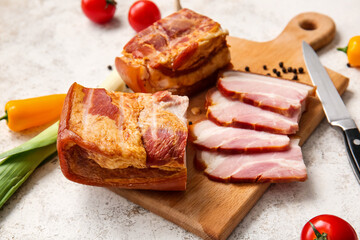 Wooden board with tasty smoked bacon on light background
