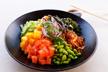 healthy poke bowl with edamame, salmon, wakame seaweed, mango, radish, cucumber, onion and rice served with sweet soy sauce, japanese food speciality