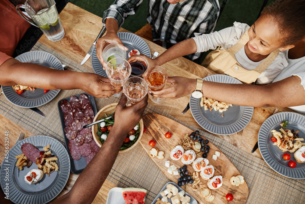 Wall mural Top down portrait of big African-American family clinking glasses while enjoying dinner together outdoors and celebrating