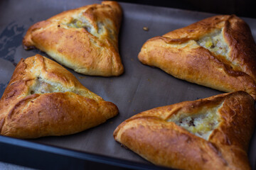 
Photo of four ruddy triangular pies on a baking sheet, just taken out of the oven