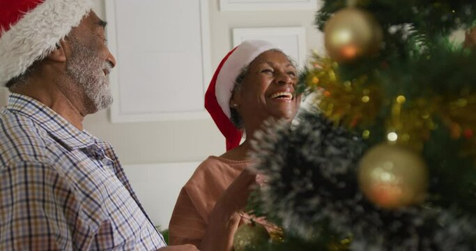 Animation of happy african american senior couple decorating christmas tree together