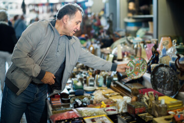 Positive senior man choosing vintage handicrafts at flea market