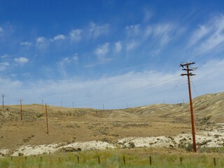 Soft cotton wads of clouds over rolling hills and power poles along the road in Wyoming