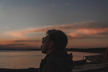 Young man making a gum balloon with his mouth while watching the sunset on the abandoned beach.