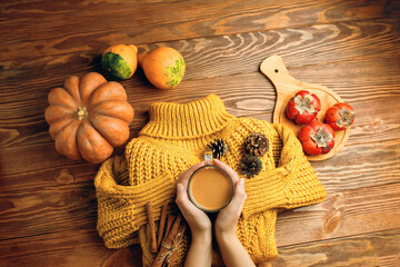 Cup of tea with milk, pine cones and cinnamon sticks on knitted sweater. Orange jacket, pumpkins and sweet persimmon on wooden background. The concept of thanksgiving. Autumn composition.