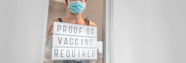 Vaccination proof and mask required to enter stores and non essential businesses as coronavirus restriction. Employe putting requirement sign in window of storefront - obrazy, fototapety, plakaty