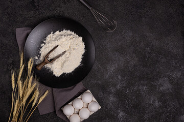White wheat flour in a wooden spoon on a dark structural background on a plate made of black stone