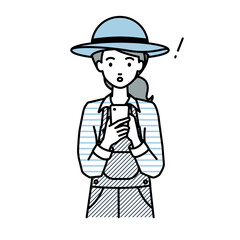 立ってスマートフォンを操作して何かに気づいて驚いた農家の女性