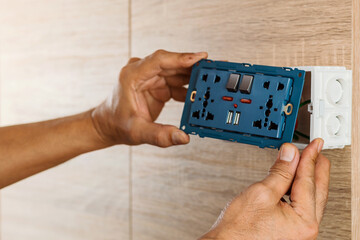 Hand of an electrician are installing the universal wall outlet AC power plug with USB port and on-off in a plastic box on a wooden wall.