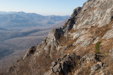View from above. Autumn forest in the Primorsky Territory. View from the top of Mount Sakharnaya near Dalnegorsk on a steep rocky ridge. Steep rock in the autumn forest.