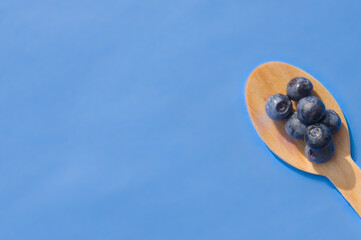 Flat lay of recycled spoon and juicy fresh blueberries on color table. Space for text. Isolated ripe sweet bilberry fruits in eco spoon on sky blue background. Copy Space. Healthy raw vegetarian food 