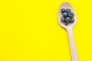 Flat lay of recycled spoon and juicy, fresh blueberries on color table. Space for text. Isolated ripe sweet bilberry fruits in eco spoon on yellow background. Copy Space. Healthy raw vegetarian food 