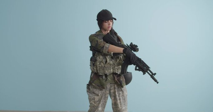 Young female soldier with assault rifle on color background