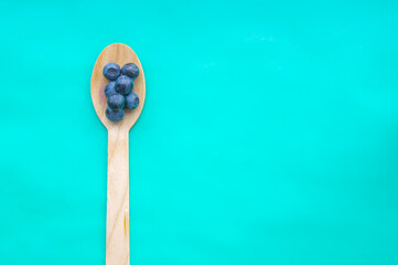 Flat lay of recycled spoon and juicy fresh blueberries on color table. Space for text. Isolated ripe sweet bilberry fruits in eco spoon on turquoise background. Copyspace. Healthy raw vegetarian food 
