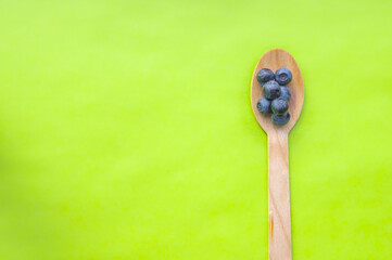 Flat lay of recycled spoon and juicy, fresh blueberries on color table. Space for text. Isolated ripe sweet bilberry fruits in eco spoon on green background. Copy Space. Healthy raw vegetarian food 