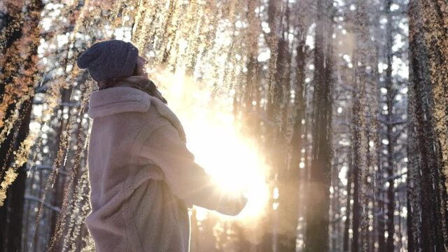 Beautiful woman on a frosty snowy day throws boiling water into the air in the forest, having fun outdoors on a sunny winter day. Winter fun.