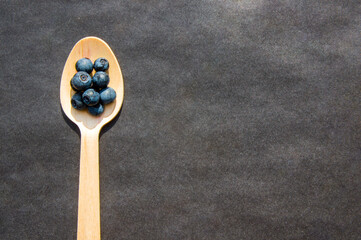Flat lay of recycled spoon and juicy fresh blueberries on rough table. Space for text. Isolated ripe sweet bilberry fruits in eco spoon on black background. Copyspace. Healthy raw vegetarian food 