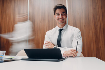 Businessman using laptop sit at table in office meeting background with walking people with motion blur. Business people man and woman group conference discussion.