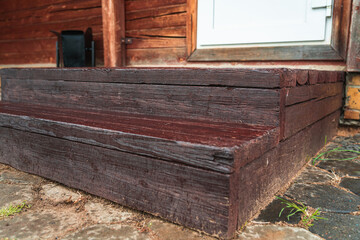 Brown wooden steps on the porch of the house, a plastic door and an urn next to it, close-up