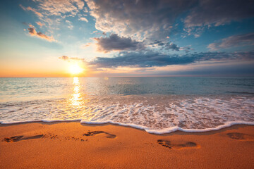 Footsteps on the beach sand and dramatic sunrise - obrazy, fototapety, plakaty