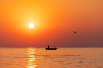 Fototapeta premium Silhouette of fisherman in a boat and norning sunrise