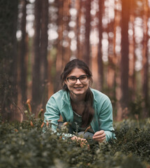 Happy girl is wearing glasses collecting berries in the forest looking into the camera. Portrait of...