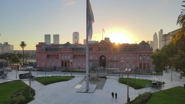 Aerial Drone Scene flying back of Casa Rosada, Buenos Aires, Argentina, the presidential pink house, the flag and the May Pyramid. Warm dawn morning sun backlight flare and reflections.
