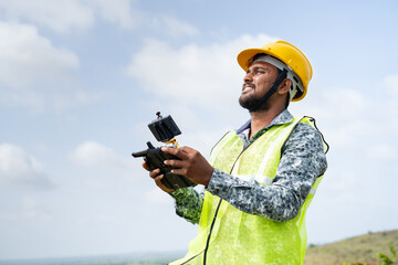 Drone pilot with safety helmet operating drone using remote controller - concept of engineer using drone technology to survey land. - obrazy, fototapety, plakaty
