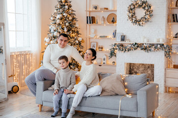 Happy beautiful family with a small son sitting on the couch in the house on the background of the Christmas tree - 458666900